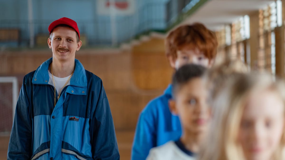 Smiling male coach guiding children in a gym setting during a physical education class.